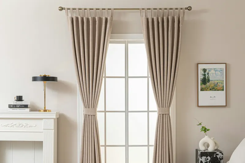 Cortinas de lino beige con tiras en la parte superior frente a una ventana luminosa, en una sala de tonos neutros