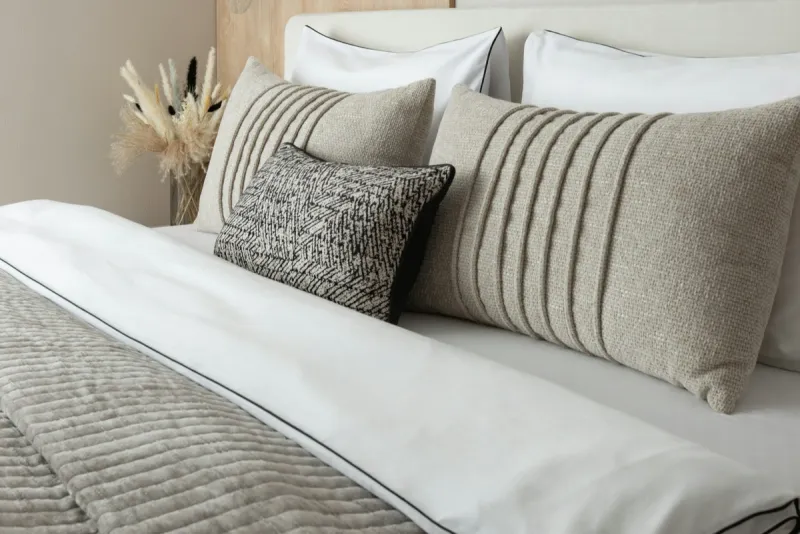 Cama con edredón blanco, cojines de lino beige y cubrecama acolchado en tonos neutros