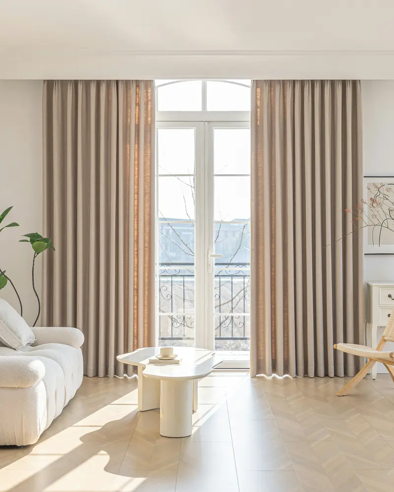 Cortinas de lino color arena junto a un ventanal en una sala luminosa y minimalista: lavado de cortinas y alfombras