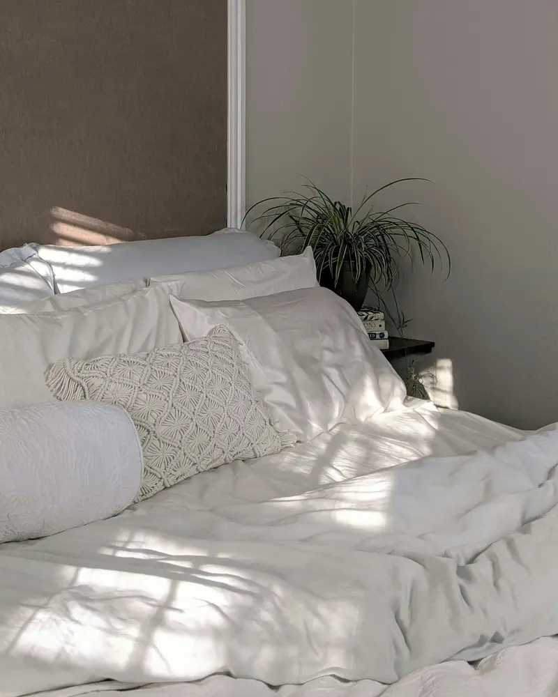 Cama con edredón blanco, almohadas y luz natural: lavado de edredones y ropa de cama