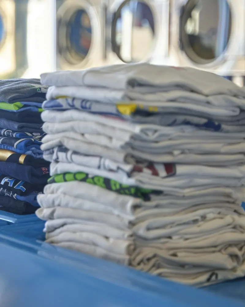 Pilas de camisetas dobladas sobre una mesa de lavandería: lavado al peso y planchado