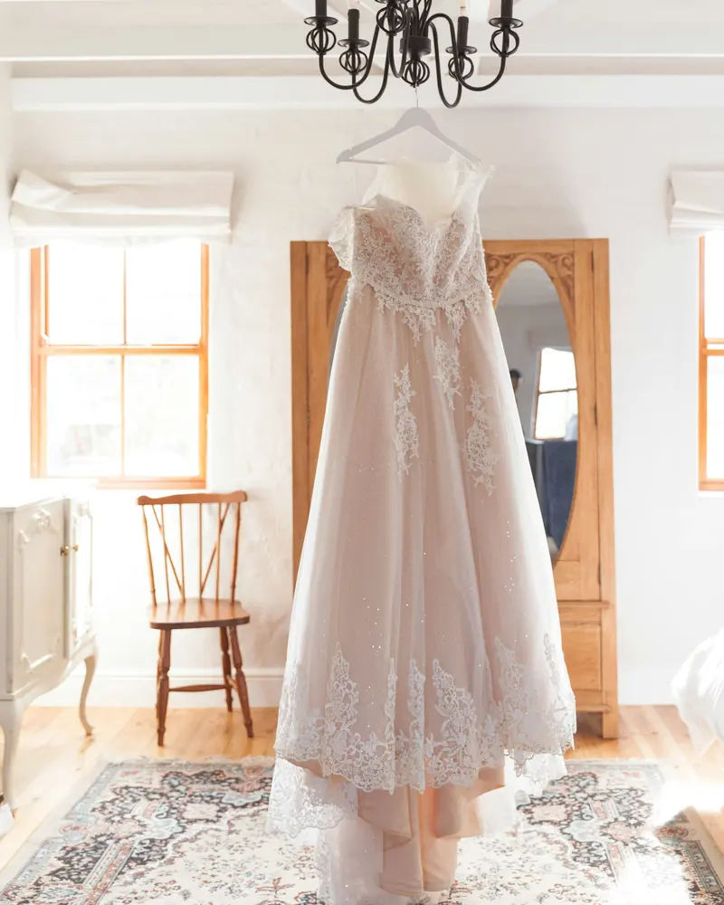 Vestido de novia de encaje y tul colgado en una habitación luminosa con ventana: limpieza de vestidos de novia