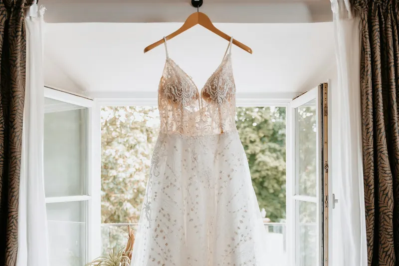 Vestido de novia de encaje y tul colgado de una percha de madera junto a una ventana: limpieza de vestidos de novia y de fiesta